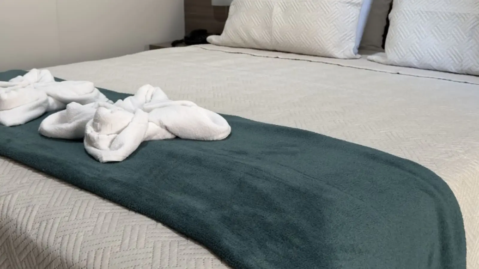 Cama Queen do Apto Luxo com enxoval branco e manta verde